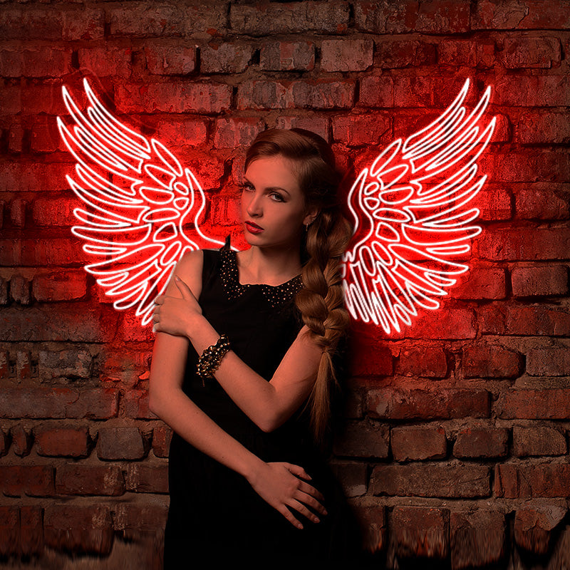 Edgy girl dressed in black posing infront of a red detailed wings LED neon sign which is installed on a brick wall.