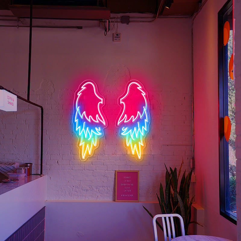 Three coloured Angel Wings LED neon sign installed on a white brick wall inside of a cafe. 
