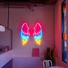 Three coloured Angel Wings LED neon sign installed on a white brick wall inside of a cafe. 