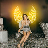 Girl at a party with a disco ball on her lap is sitting on a chair posing infront of a golden yellow ascended Angel Wings LED neon sign